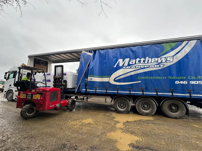 Red forklift loading cargo onto a blue Matthews delivery truck at an industrial yard
